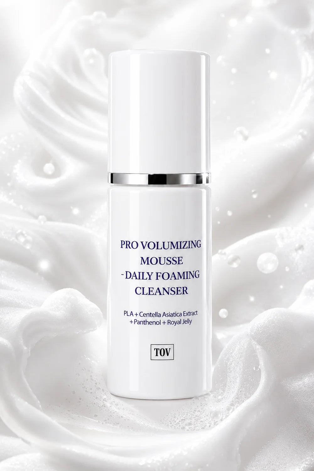 A white cylindrical skincare bottle labeled 'PRO VOLUMIZING MOUSSE - DAILY FOAMING CLEANSER' with a silver band and the brand 'TOV' at the bottom, set against a white whipped cream background with droplets.